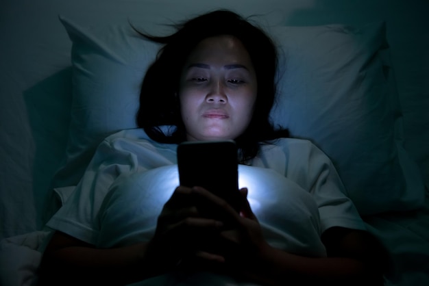 Mulher asiática jogando no smartphone na cama à noiteTailândiapessoasViciado mídia social