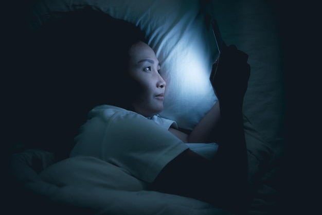 Mulher asiática jogando no smartphone na cama à noiteTailândiapessoasViciado mídia social