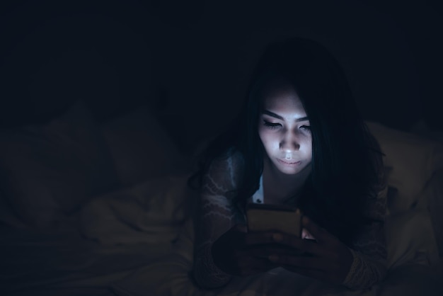 Mulher asiática jogando no smartphone na cama à noiteTailândiapessoasViciado mídia social