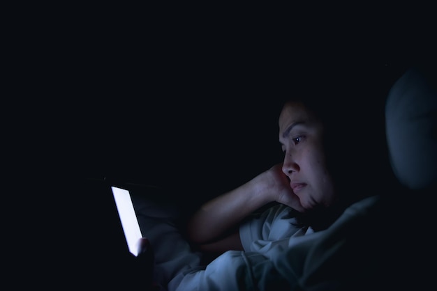 Mulher asiática jogando no smartphone na cama à noitetailândiapessoasviciado mídia social