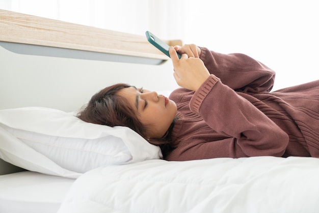 Mulher asiática jogando smartphone na cama