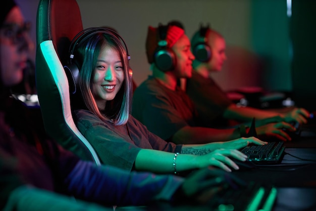 Mulher asiática jogando videogames e sorrindo na equipe de esportes cibernéticos