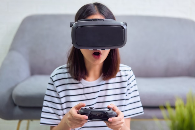 Mulher asiática jovem animada usando um fone de ouvido de realidade virtual e joysticks, conexão de conceito e interfaces de tecnologia digital.