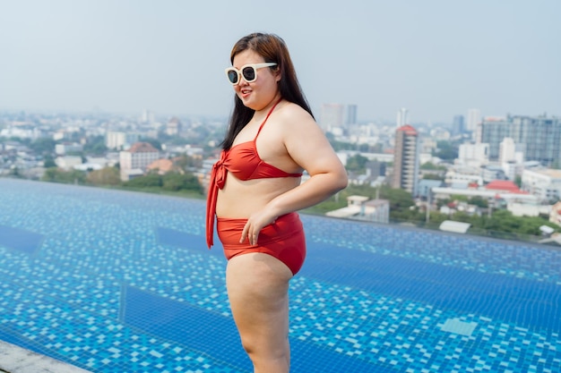 Mulher asiática jovem com excesso de peso vestindo fato de banho relaxando na piscina feliz mulher plus size alegre engraçada férias viajando no verão