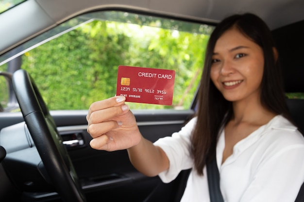Mulher asiática jovem feliz dirigindo um carro e segurando um cartão de crédito na mão