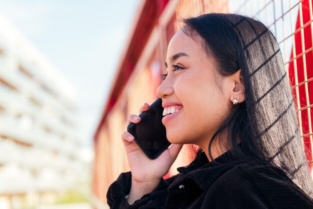 Mulher asiática jovem feliz sorrindo enquanto fala ao telefone ao ar livre