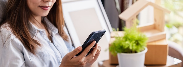 Mulher asiática jovem feliz usando smartphone com uma pilha de caixas de papelão