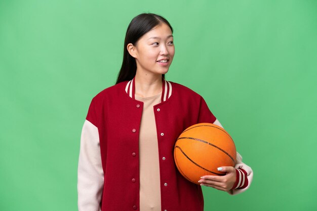 Mulher asiática jovem jogador de basquete sobre fundo isolado, olhando de lado