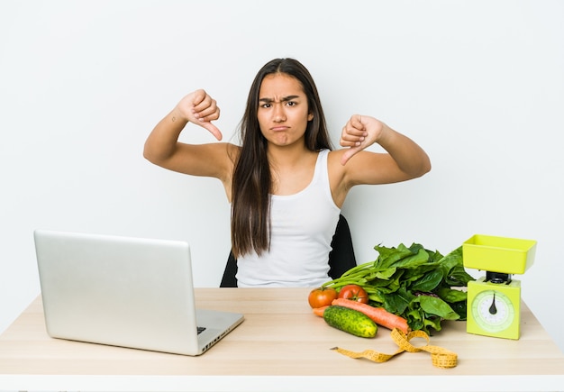 Mulher asiática jovem nutricionista isolada na parede branca mostrando o polegar para baixo e expressando antipatia