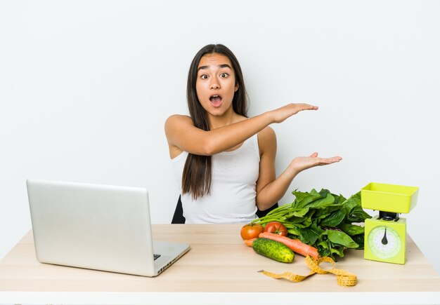 Mulher asiática jovem nutricionista isolada no branco chocada e espantada, segurando um espaço de cópia entre as mãos.