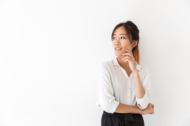 Mulher asiática jovem sorridente atraente vestindo camisa isolada, pensando, olhando para longe