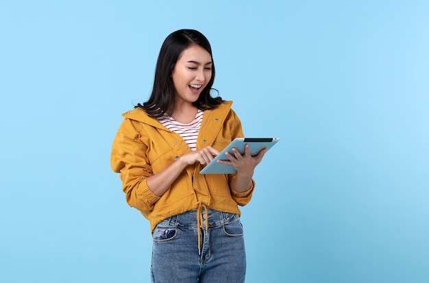 Mulher asiática jovem sorridente usando um computador tablet isolado na parede azul