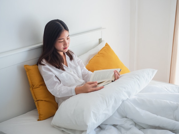 Mulher asiática lendo livro na cama de manhã