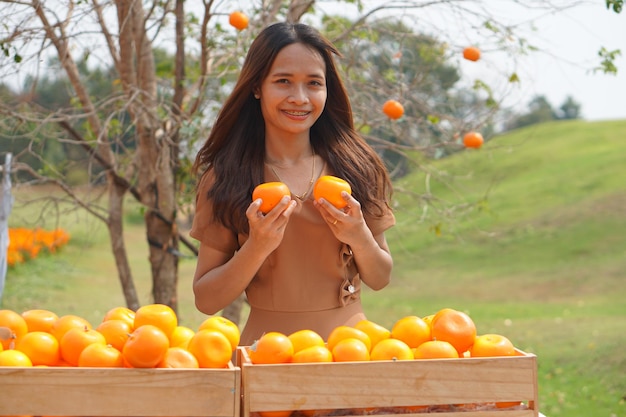 Mulher asiática levantando uma cesta de laranjas em um campo