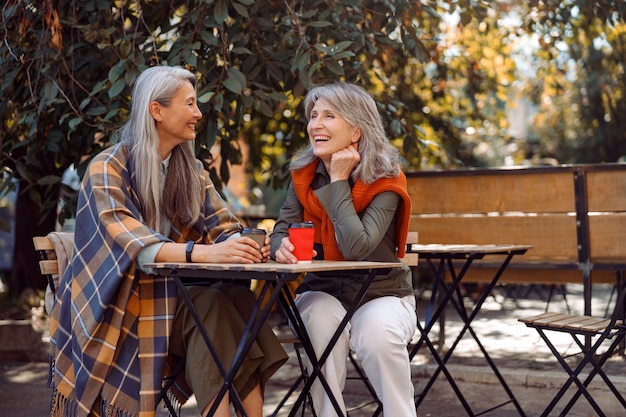 Mulher asiática madura com um amigo positivo de cabelos grisalhos passam um tempo juntos em um café de rua