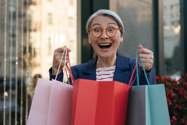 Mulher asiática madura e feliz segurando sacolas de compras perto do conceito de vendas da Black Friday