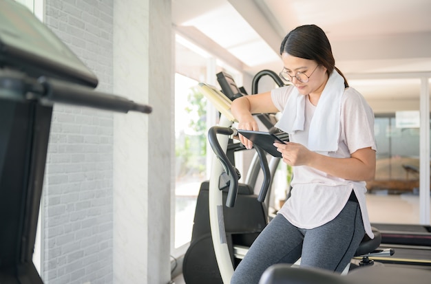 Mulher asiática malhando e trabalhando online sozinha na GYM. Distanciamento social e novo estilo de vida normal.