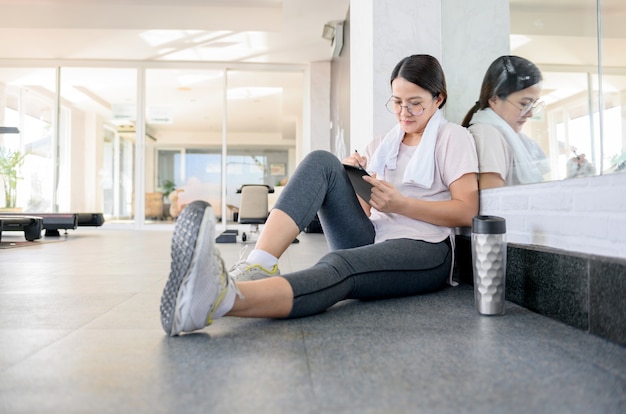 Mulher asiática malhando e trabalhando online sozinha na GYM. Distanciamento social e novo estilo de vida normal.