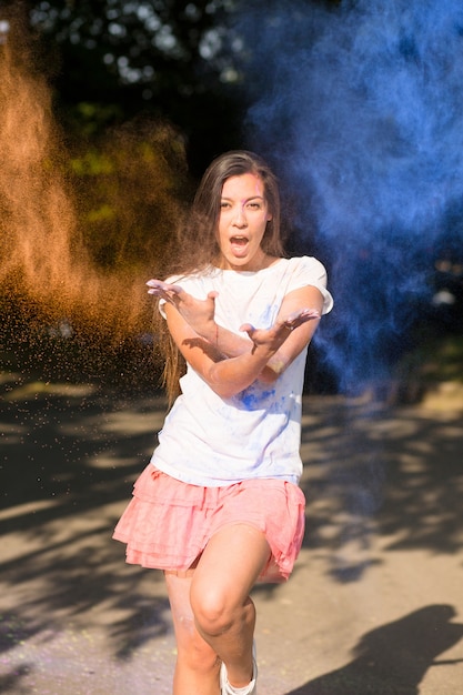 Mulher asiática morena expressiva brincando com tinta Holi explodindo ao seu redor