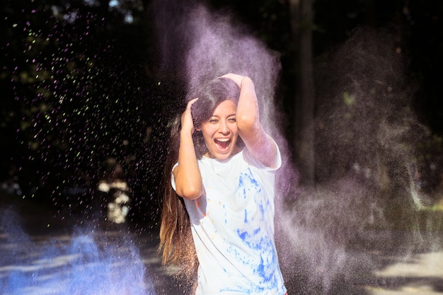 Mulher asiática morena sorridente com cabelo comprido brincando com tinta roxa de Holi