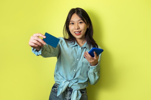 Mulher asiática, mostrando o cartão de crédito usando o fundo amarelo de compras de celular