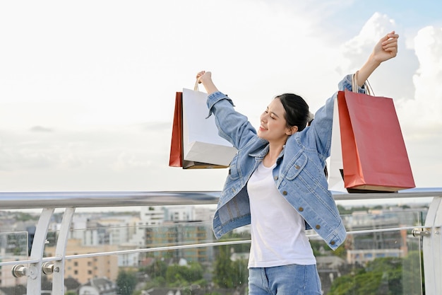 Mulher asiática muito feliz carregando suas sacolas de compras gosta de fazer compras no shopping da cidade