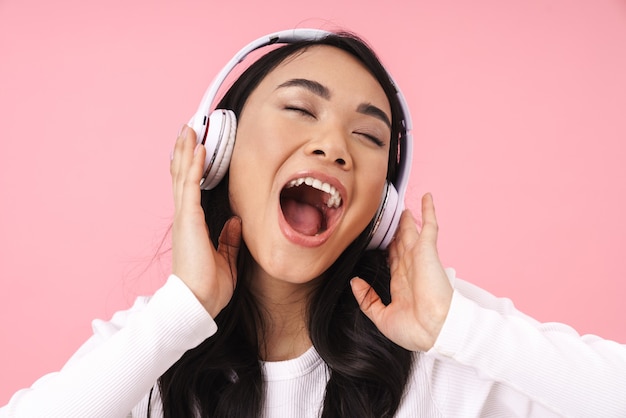 Mulher asiática muito jovem alegre ouvindo música com fones de ouvido sem fio isolados, cantando