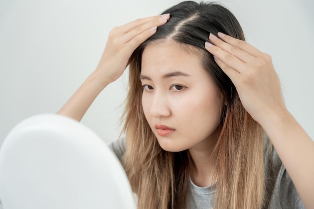 Foto mulher asiática muito triste e chateada olhando para cabelos danificados, perda de cabelo, problema de queda de cabelo