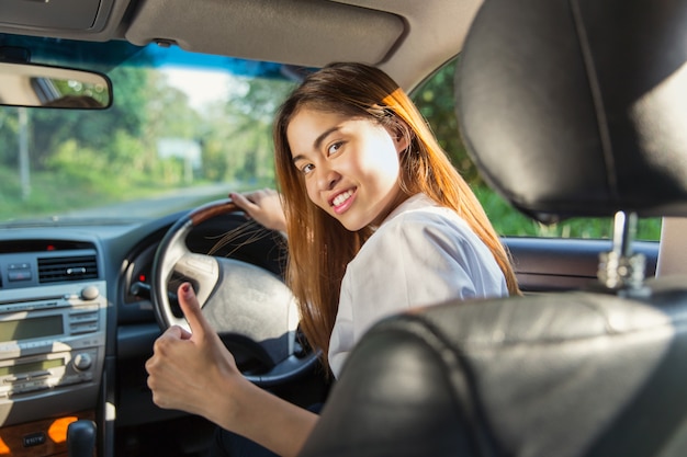 Mulher asiática nova de sorriso que senta-se no carro