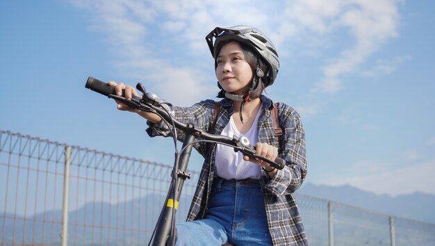 Mulher asiática nova passeio de bicicleta no fundo do céu azul