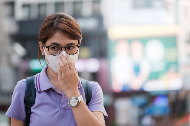 Mulher asiática nova que veste a máscara da proteção contra o vírus da gripe na cidade. conceito de saúde e poluição do ar