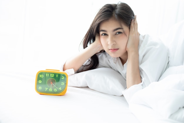 Foto mulher asiática odeia acordar cedo de manhã. menina sonolenta, olhando para o despertador