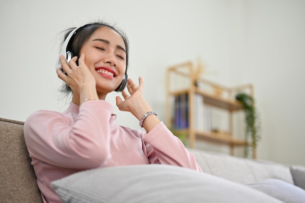 Mulher asiática pacífica e relaxada usando fones de ouvido com os olhos fechados se divertindo com a música