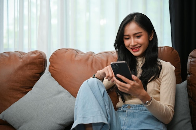 Mulher asiática passando seu fim de semana em casa socializando com seus amigos em seu smartphone