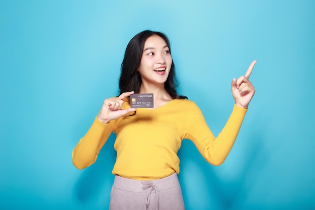 Mulher asiática posando com um cartão de crédito Retrato de uma bela jovem em um fundo azul claro feliz e sorridente posando em posição de pé