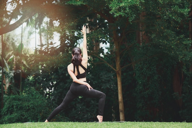 Mulher asiática praticando ioga em warrior pose virabhadrasana no tapete no parque ao ar livre