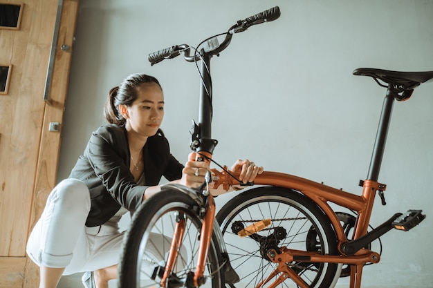 Mulher asiática prepara uma bicicleta dobrável de sua casa para ir ao trabalho