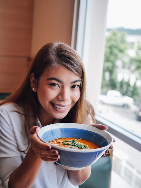 Foto mulher asiática que guarda a sopa picante do macarronete nas mãos no restaurante.