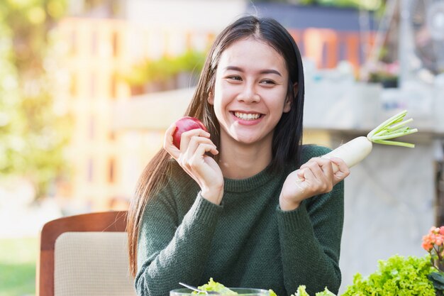 Mulher asiática que guarda vegetais e fruto que levanta com feliz.