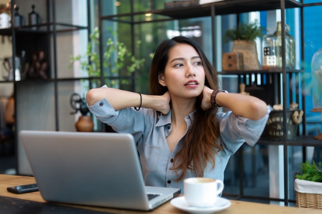 Mulher asiática que trabalha e bebe café no café com sorriso de computador portátil e trabalho feliz