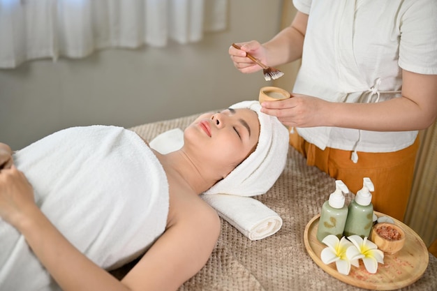 Mulher asiática relaxada deitada na mesa de massagem com os olhos fechados recebendo tratamento facial