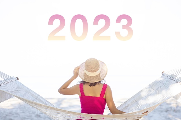 Mulher asiática relaxando na rede na praia tropical em 2023 desfruta de sua liberdade e ar fresco usando chapéu e roupas elegantes Turista sorridente feliz nos trópicos em férias de viagem