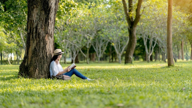 Mulher asiática relaxando sentada feliz lendo um livro no parque