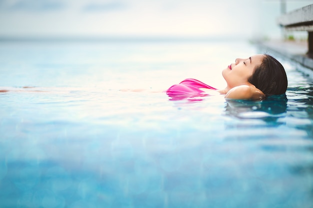 Mulher asiática relaxar na piscina na praia