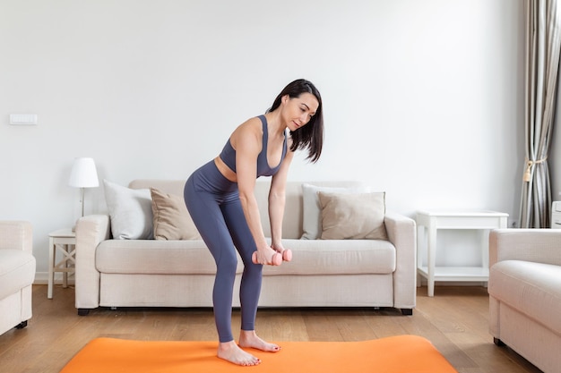 Mulher asiática se exercita com halteres em casa Mulher feliz fazendo exercícios de braço usando halteres