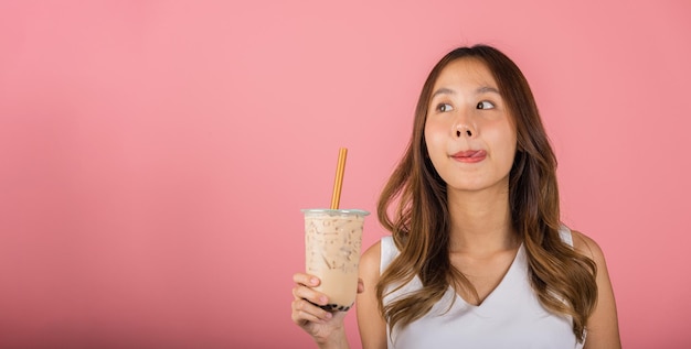 Mulher asiática segurando bebendo açúcar castanho saborizado tapioca pérola bolha de leite chá lamber lábios querem provar têm deliciado férias de verão sonho sorriso feminino isolado em fundo rosa conceito de bebida