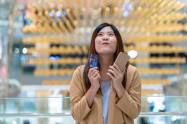 Mulher asiática, segurando o cartão de crédito e telefone celular para compras on-line