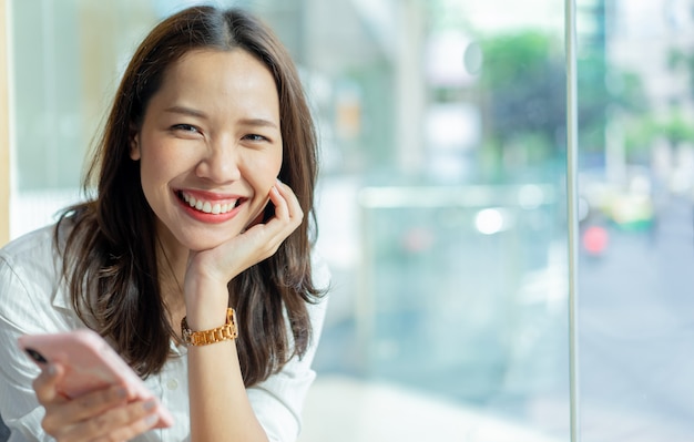 mulher asiática, segurando o smartphone para reproduzir o conteúdo do aplicativo na rede de mídia social no café café