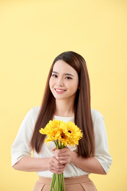 Mulher asiática segurando um ramo de flores encostada na parede