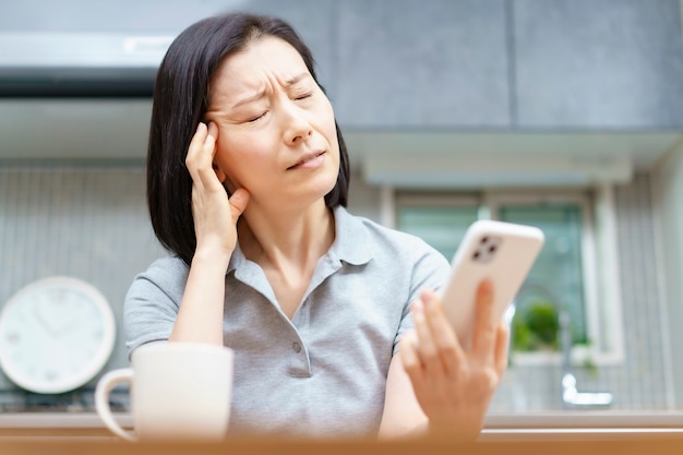 Mulher asiática segurando um smartphone com um olhar cansado na sala